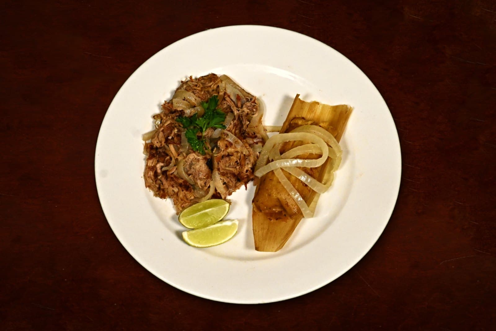 Tamal con Lechón: roast pork, sautéed onions, lime, plated on a dark wood table