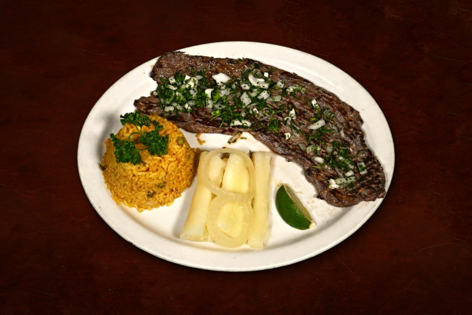 Bistec de Palomilla: grilled thin-cut steak, yellow rice, yuca, plated on a dark wood table